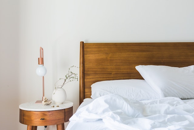 bed with a wooden frame and white sheets next to a night table